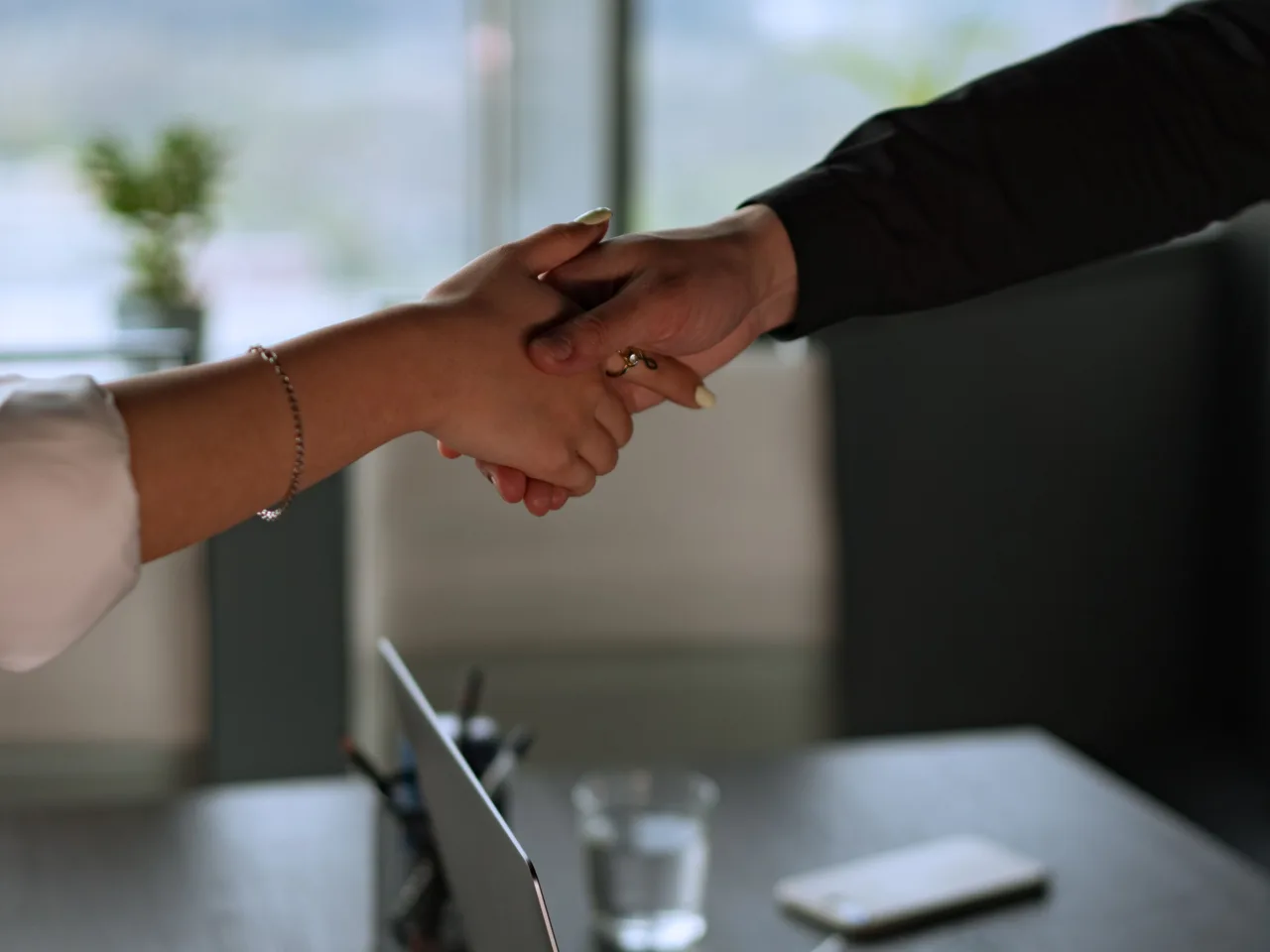 Handshake across a desk with a laptop